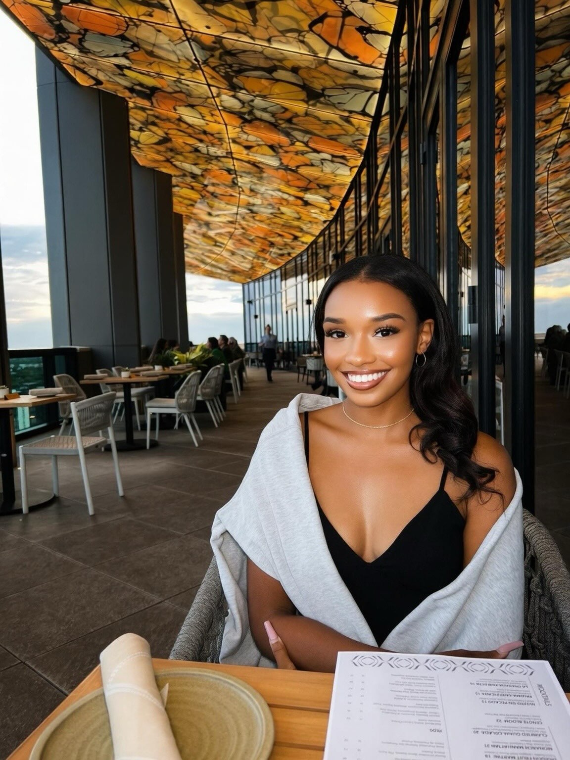 Nayla smiling at a table beneath a glowing ceiling of amber butterfly wings